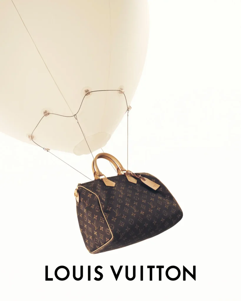Angled view of a Louis Vuitton Speedy monogram handbag hanging beneath a white balloon, highlighting the bag's rounded silhouette, leather trim, and floating present