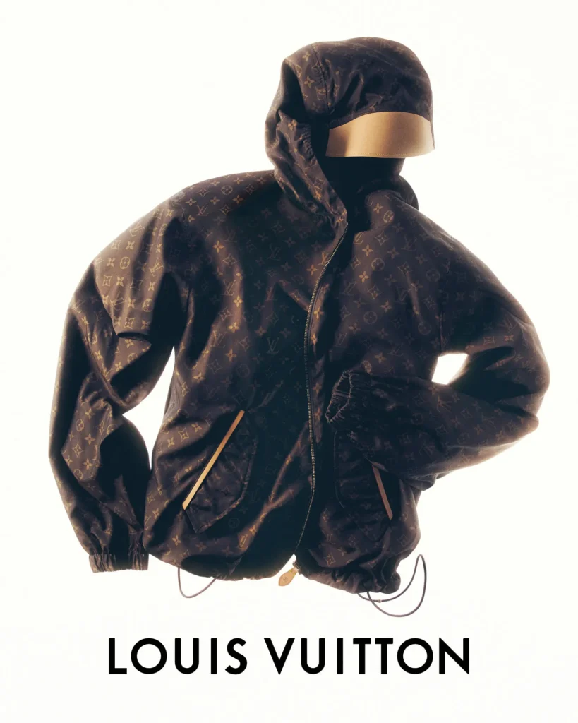 Brown Louis Vuitton monogram hooded technical jacket displayed on a headless mannequin with a gold visor, featuring oversized proportions, zip front, drawcord hem, and contrasting beige trim