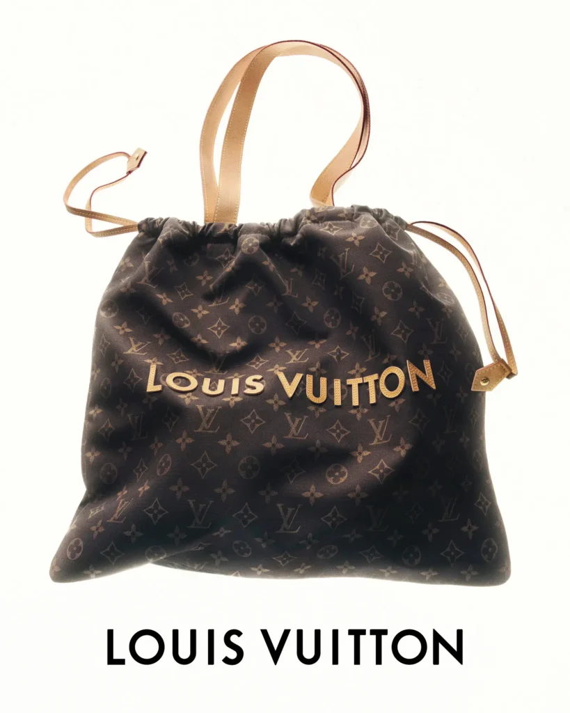 Large Louis Vuitton monogram drawstring tote bag with beige leather shoulder straps and raised gold Louis Vuitton lettering centered across the front in a clean studio photograph