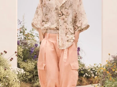 Model walking a garden runway in a relaxed floral-print short-sleeve shirt, wide blush pink cargo trousers, layered necklace, and beige sandal