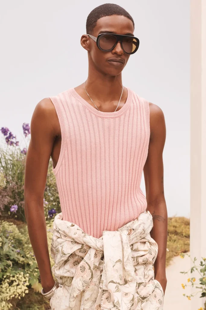 Model wearing a ribbed pastel pink sleeveless knit top, oversized black sunglasses, floral trousers tied at the waist, and silver jewelry