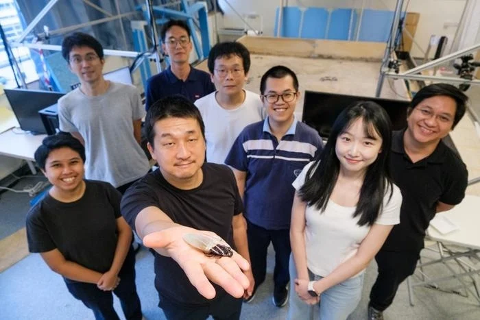 NTU Singapore researchers pose in a laboratory as one team member holds a cyborg cockroach equipped with a miniature oxygen-generating diving suit designed for underwater robotics research.
