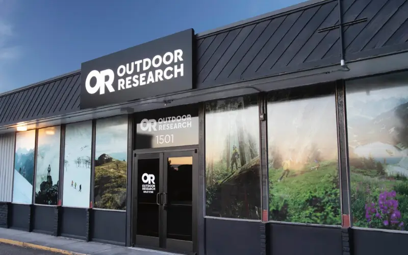 Exterior of an Outdoor Research retail store featuring large brand signage above the entrance and window displays showcasing hiking, climbing, and alpine landscapes.