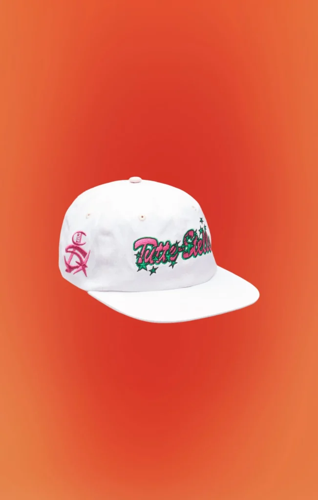White snapback cap featuring embroidered "Tattoo Studio" script in pink and green across the front, pink side logo embroidery, flat brim, and structured six-panel construction