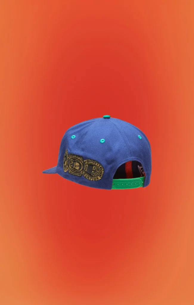 Blue snapback cap viewed from the back, featuring embroidered championship belt artwork, green snapback closure, matching green eyelets, and a flat brim