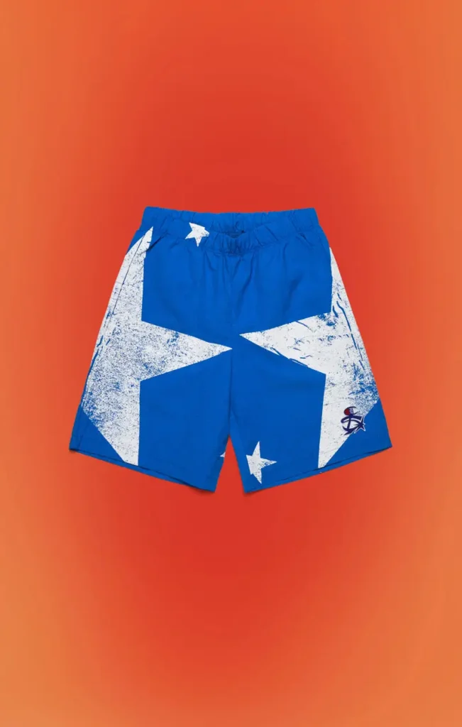 Royal blue athletic shorts featuring oversized distressed white star graphics, elastic waistband, embroidered side logo, and matching design language coordinated with the collection's outerwear