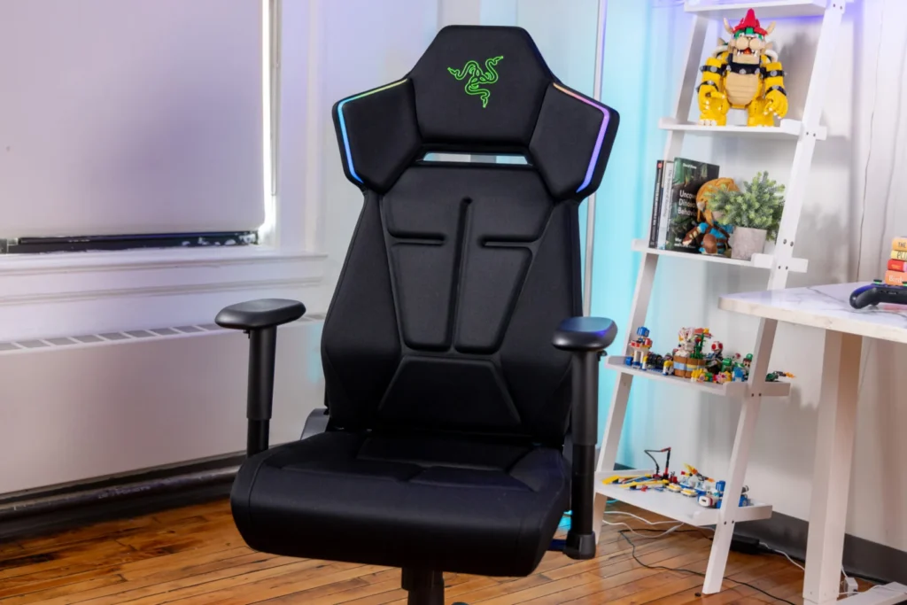 Full view of the Razer gaming chair in a modern gaming setup, showcasing its ergonomic design, adjustable armrests, and RGB-lit shoulder accent