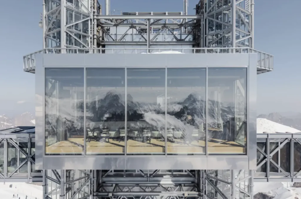 Exterior view of a glass-walled Rolex boutique suspended within a modern steel observation tower, reflecting the surrounding alpine landscape