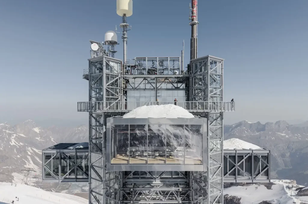 Wide shot of the elevated Rolex boutique integrated into a mountaintop observation structure surrounded by snow and panoramic mountain vista