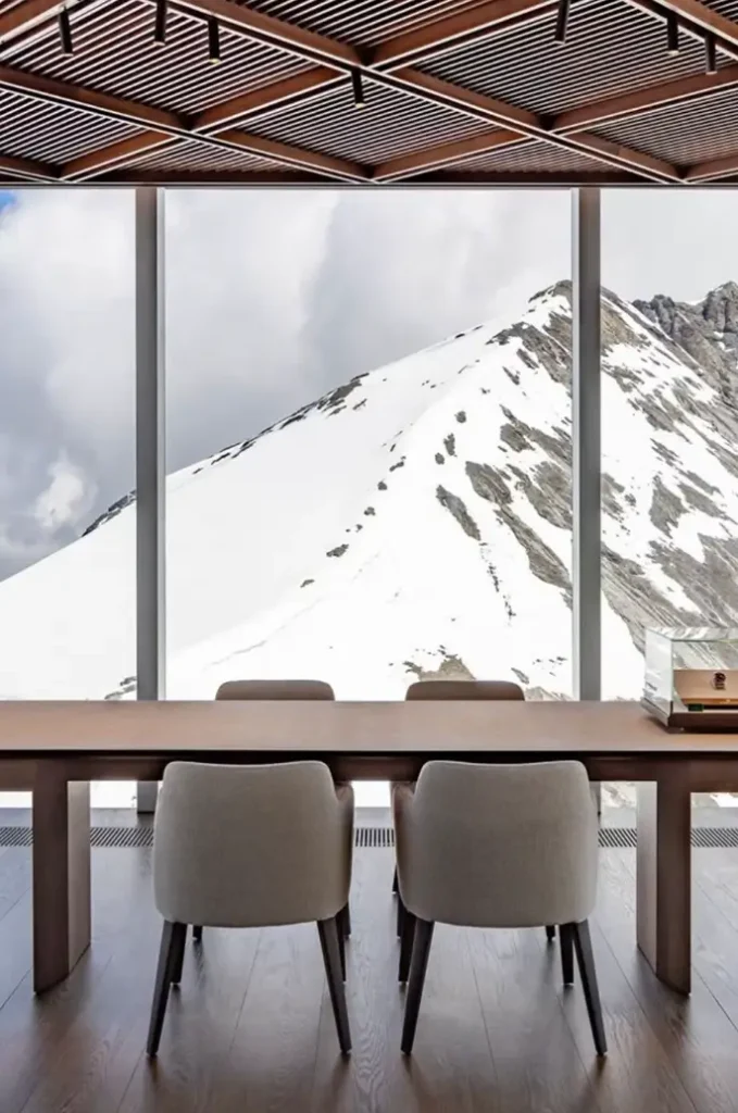 Minimalist Rolex consultation table facing floor-to-ceiling windows with breathtaking snow-covered mountain views and a single watch display case