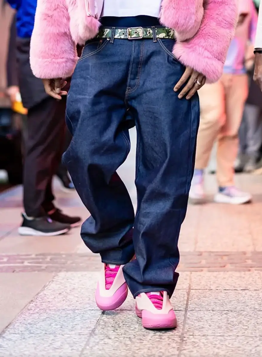 Close-up of an on-foot pink Converse SHAI basketball shoe paired with baggy dark denim jeans and a pink faux fur jacket during an arena arrival.