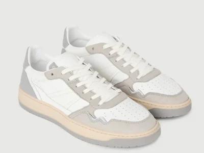 Pair of white and light gray leather low top shoe displayed at an angled front view, highlighting suede overlays, perforated toe boxes, white laces, cream midsoles, and gray rubber outsole