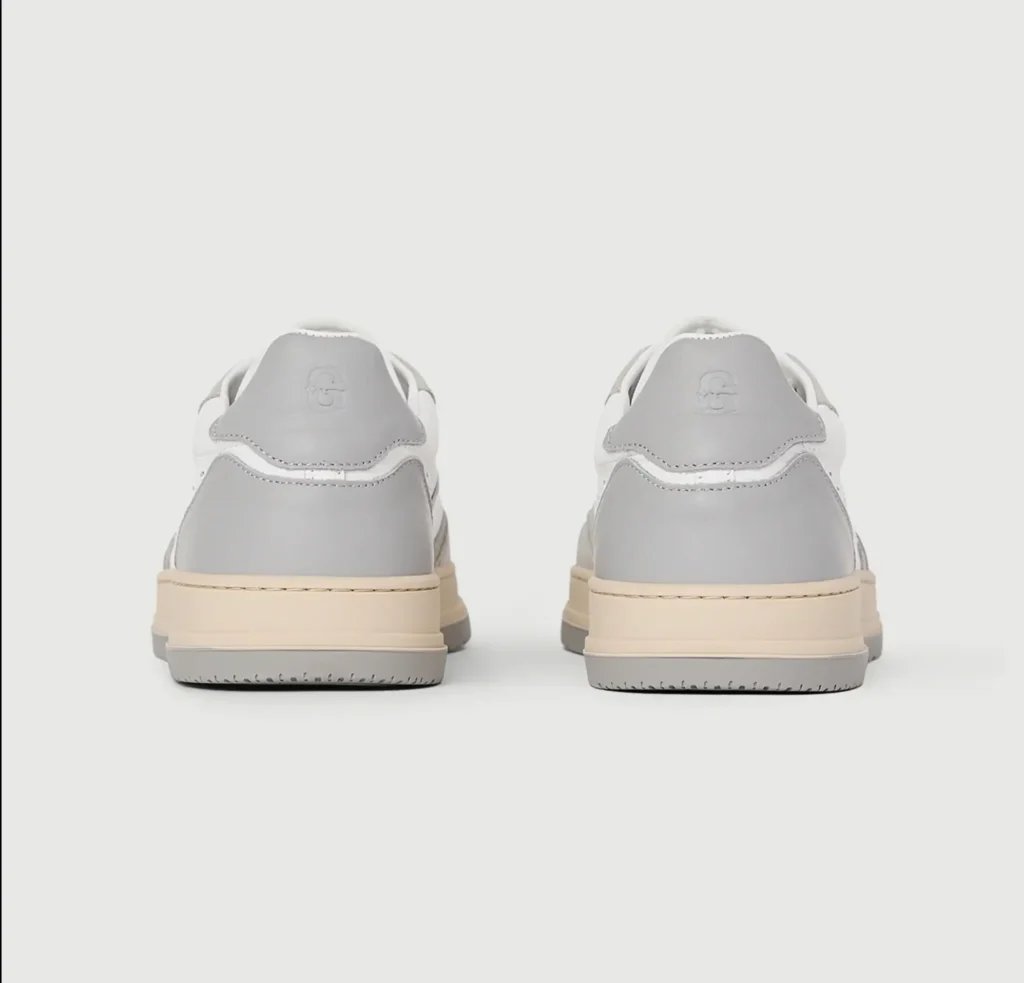 Rear view of the pair showing light gray leather heel tabs with embossed branding, white leather uppers, cream midsoles, and gray outsole
