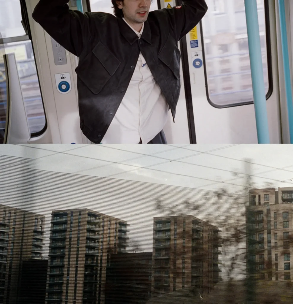 Split-frame photograph of a male model in a cropped black utility jacket holding an overhead rail inside a moving train, followed by blurred apartment blocks seen through the carriage window