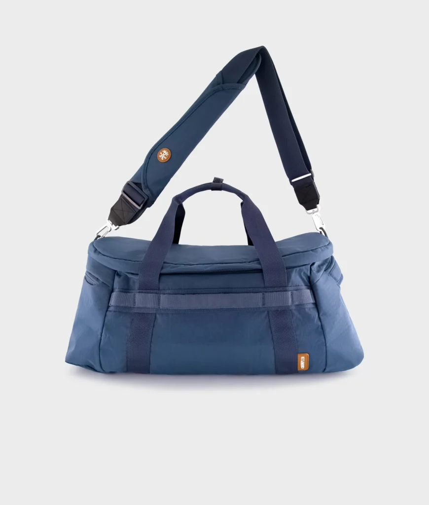 Blue Crumpler duffel bag displayed against a clean white background with dual carry handles, padded shoulder strap, and spacious travel-ready construction