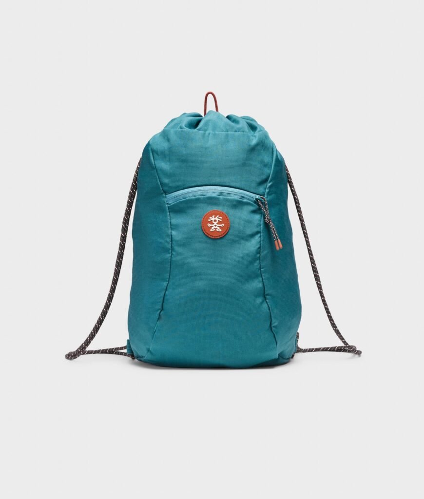 Teal Crumpler packable drawstring backpack displayed against a clean white background with front zip pocket, cord shoulder straps, and circular logo patch