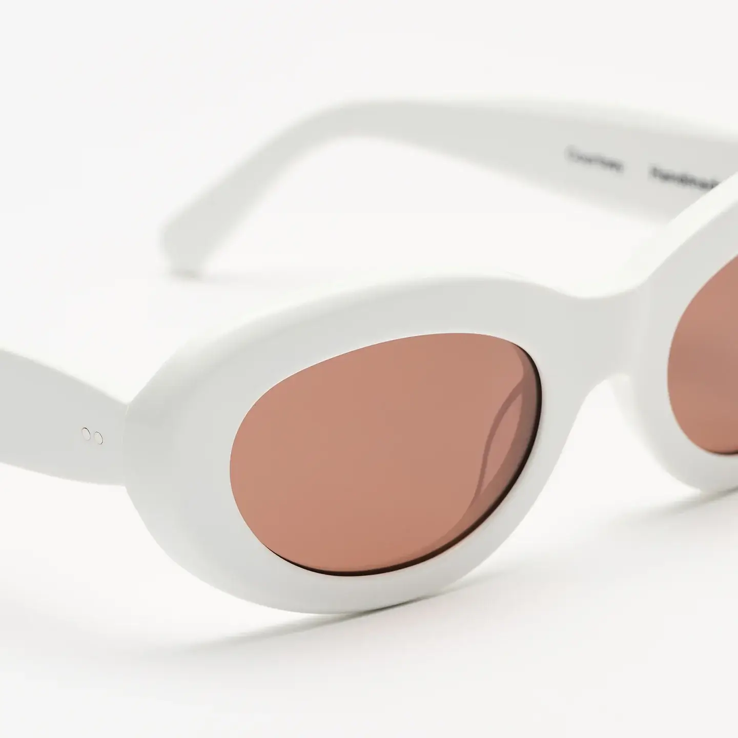 Close-up of the Sun Buddies Courtney sunglasses featuring a white oval acetate frame with soft pink-tinted lenses.