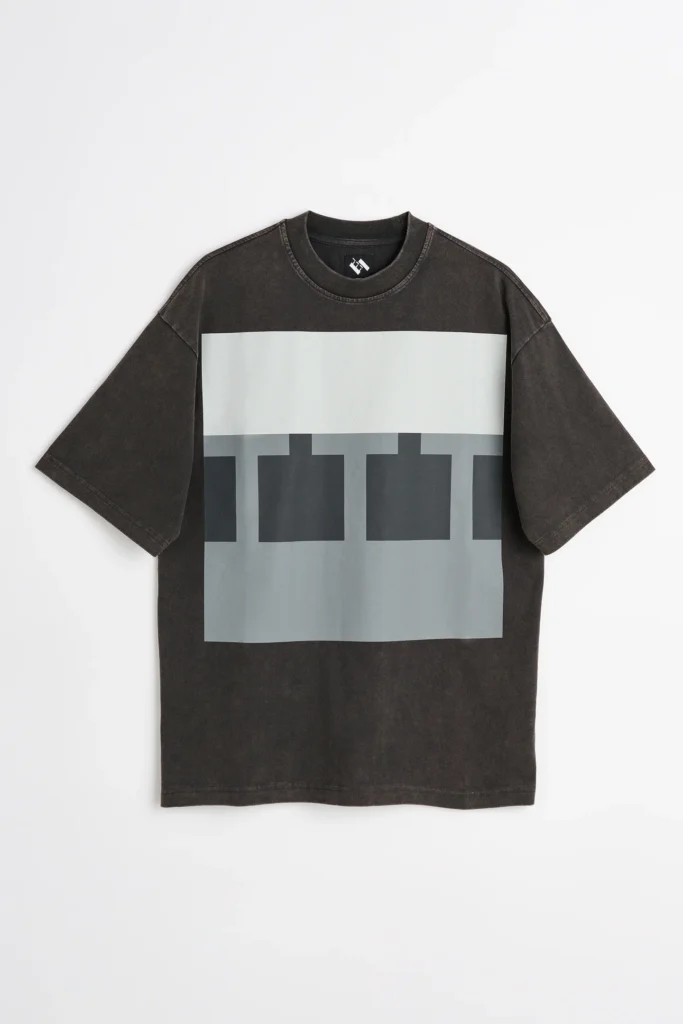 A washed black oversized Tee featuring a large geometric graphic in shades of white and gray across the chest. Presented flat against a white background, the design reflects The Trilogy Tapes' understated, experimental view language