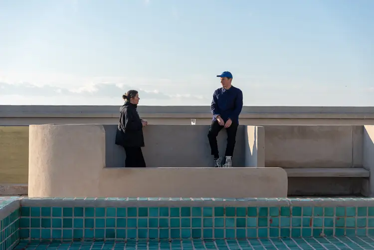 Designers from Studio CP-RV standing beside a minimalist concrete installation with a tiled pool in the foreground.