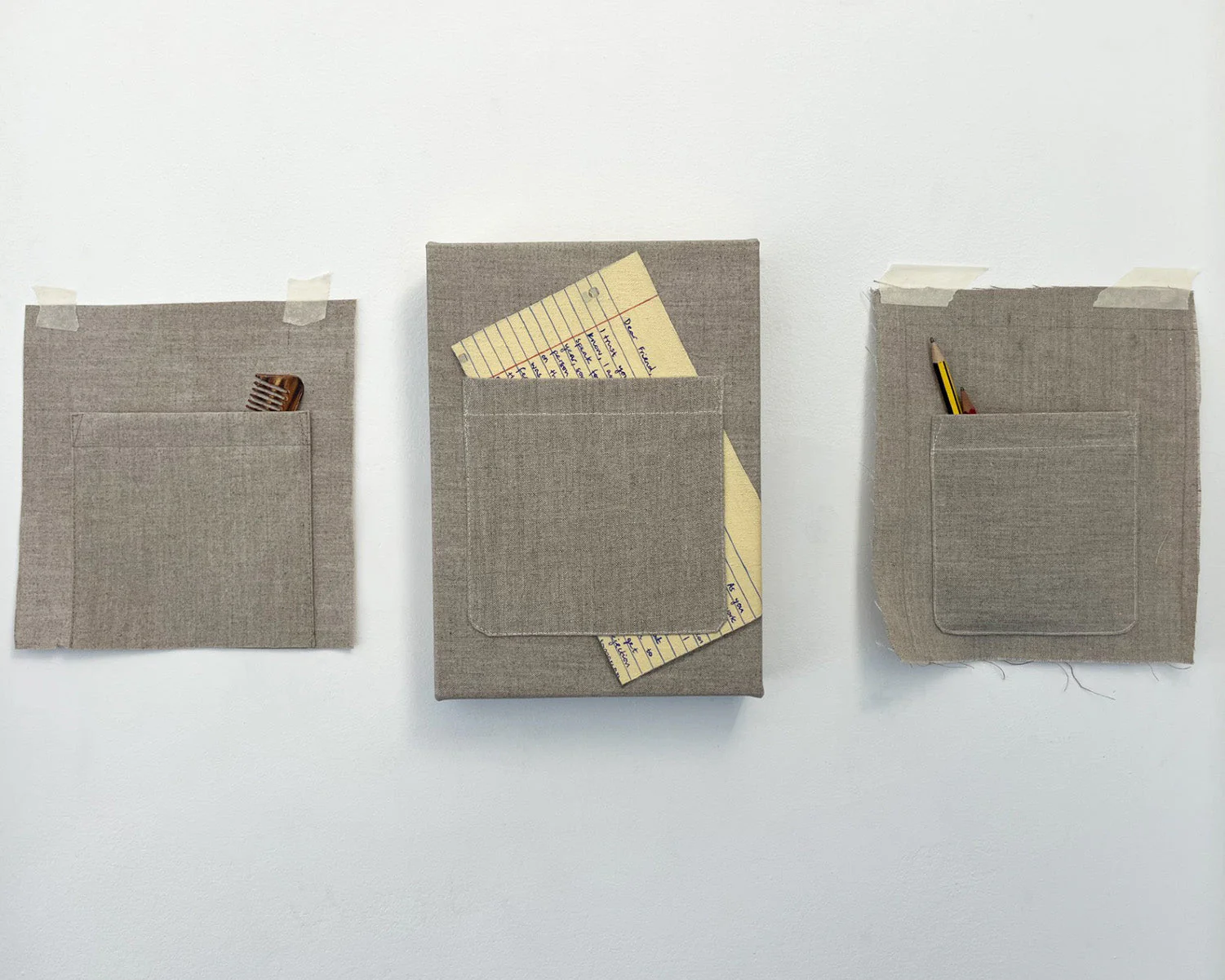 Three sewn canvas pocket studies displayed side by side, featuring fabric utility pockets holding a comb, handwritten note cards, and pencils to explore illusion, memory, and everyday objects.
