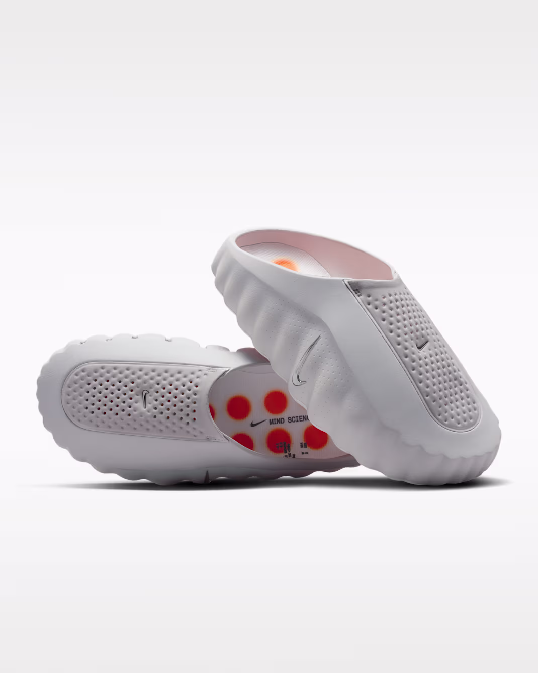 A pair of white Nike recovery slides with sculpted foam construction, perforated uppers, mini Swoosh logos, and vibrant orange dot graphics visible on the footbeds against a clean white background.