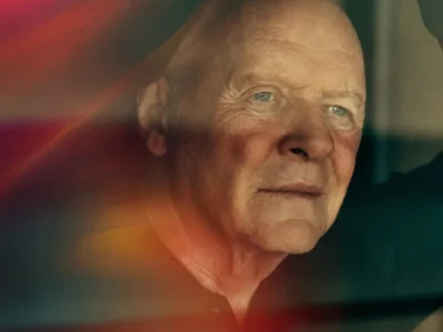 Close-up portrait of Anthony Hopkins gazing thoughtfully into the distance, his forearms resting above his head. Warm red, orange, and teal light leaks blur across the foreground, creating a cinematic, reflective atmosphere against a softly shadowed interior background