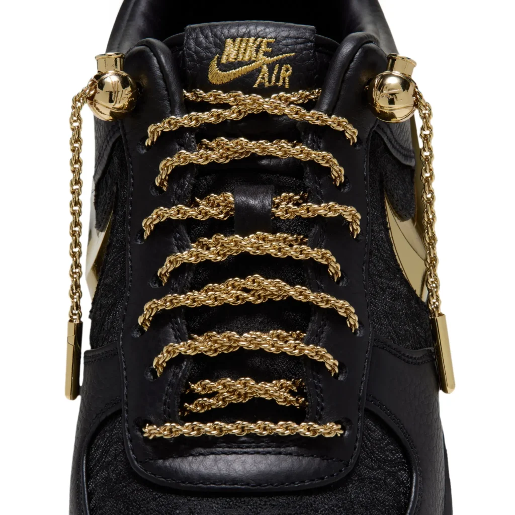 Close-up of the Nike Air Force 1 showcasing braided metallic gold chain laces, polished gold lace hardware, black leather tongue, and embroidered gold Nike Air logo