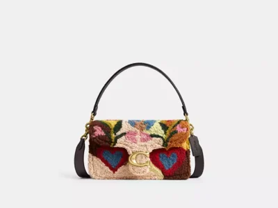 Front view of a Coach Tabby shoulder bag in multicolored shearling with floral and heart motifs, gold-tone C clasp, dark brown leather trim, and detachable shoulder strap
