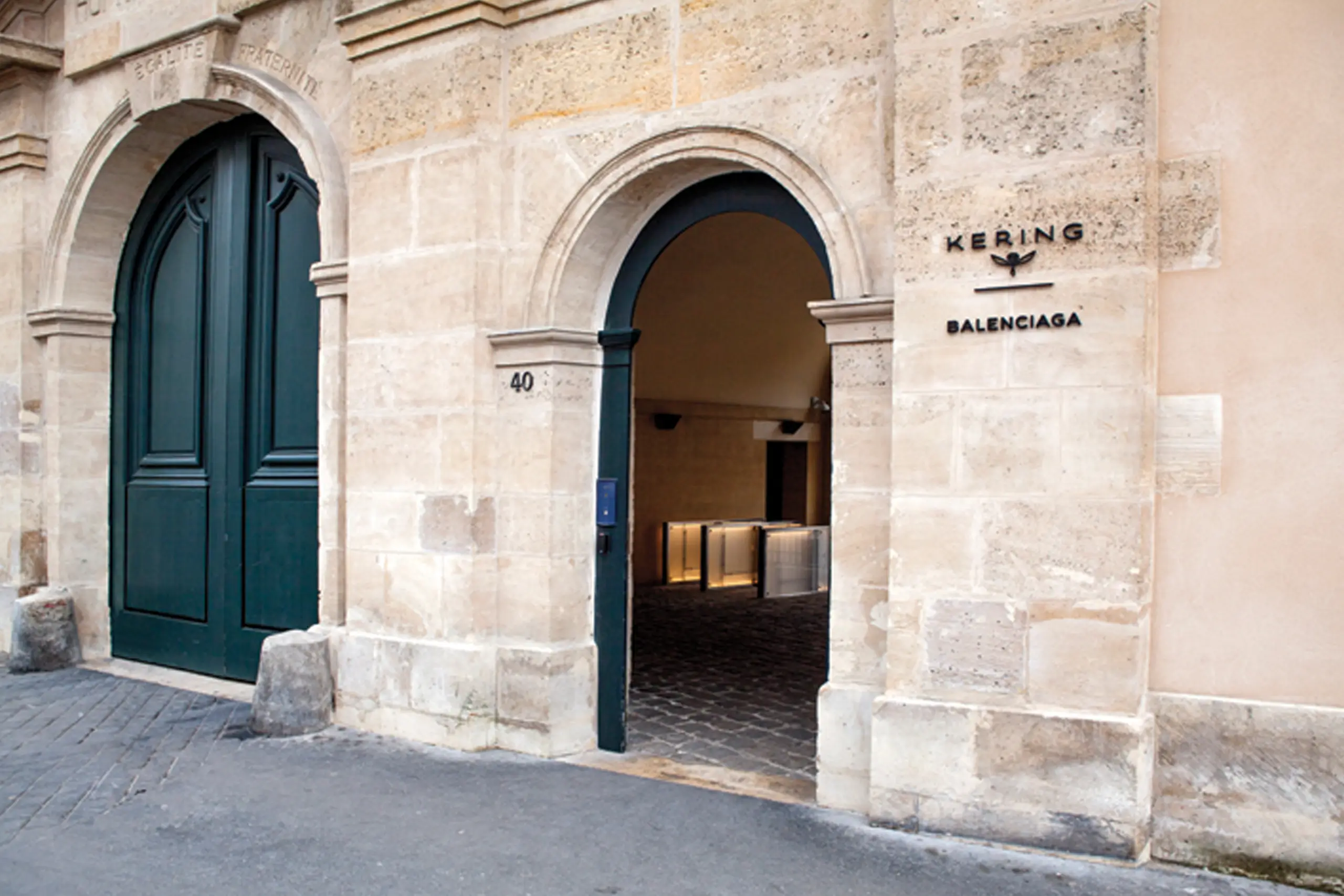 Exterior entrance to Kering's Paris headquarters at 40 Rue de Sèvres, featuring a historic limestone façade with arched doorways, dark green doors, and Kering and Balenciaga signage beside the main entrance.