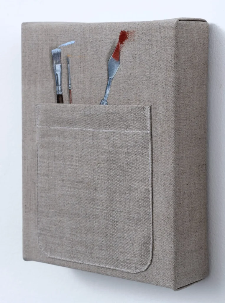 Minimalist canvas artwork with a stitched utility pocket holding an artist's paintbrush, fine detail brush, and metal palette knife tipped with red paint, highlighting realistic textile craft
