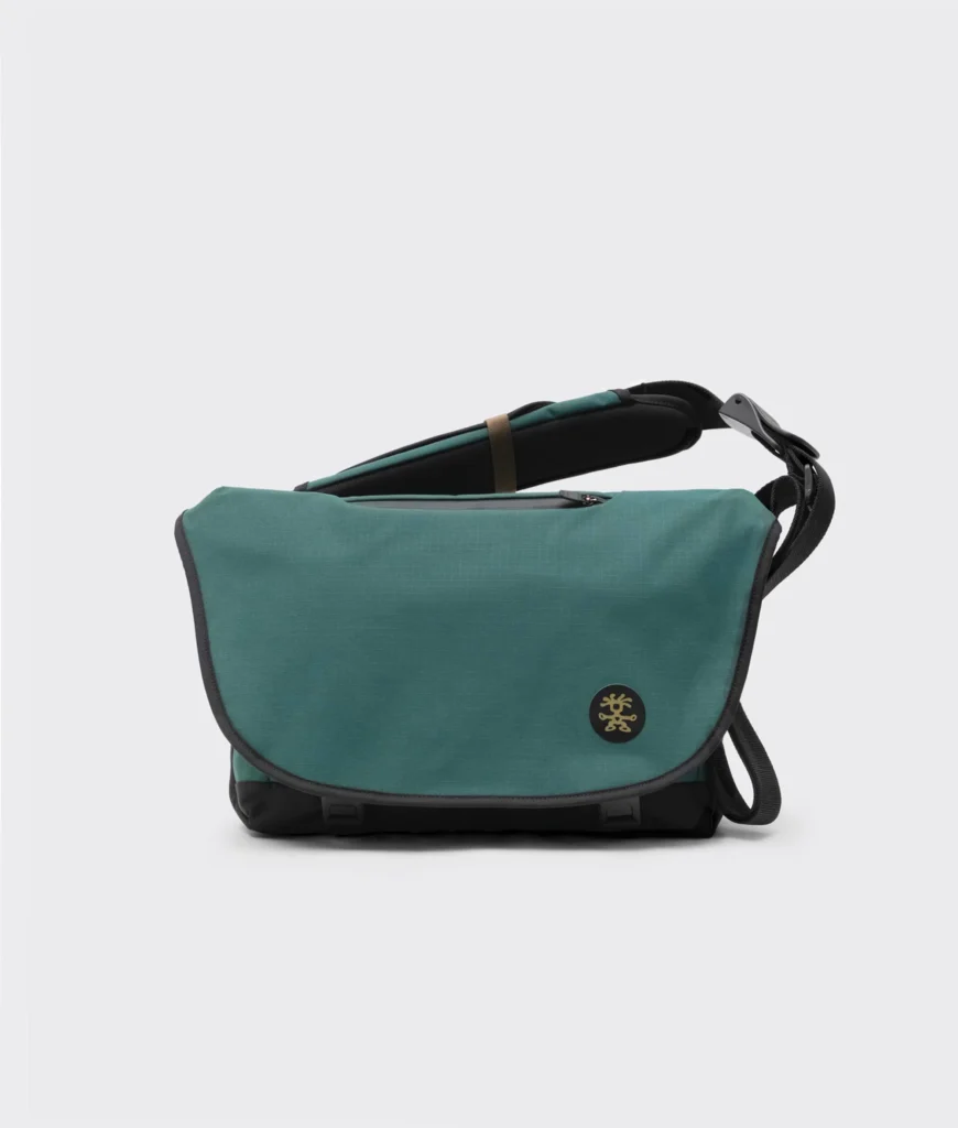 Dark teal Crumpler messenger bag photographed against a clean white background, featuring a wide flap closure, adjustable shoulder strap, and circular logo badge