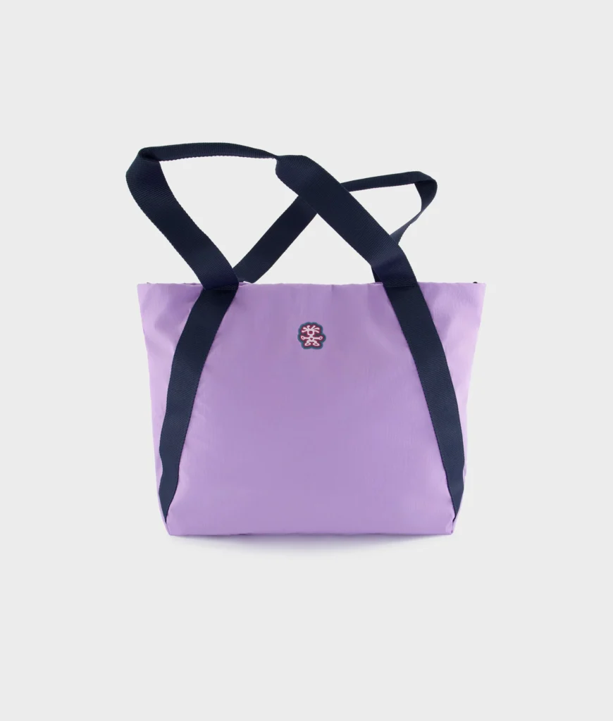 Lavender Crumpler tote bag displayed against a clean white background with navy webbing handles and a centered embroidered logo