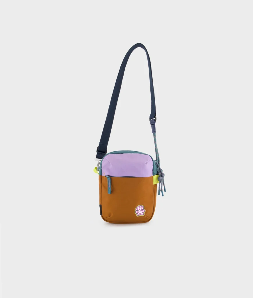 Small Crumpler shoulder pouch in camel and lavender with teal zipper pulls and adjustable strap, displayed against a clean white background