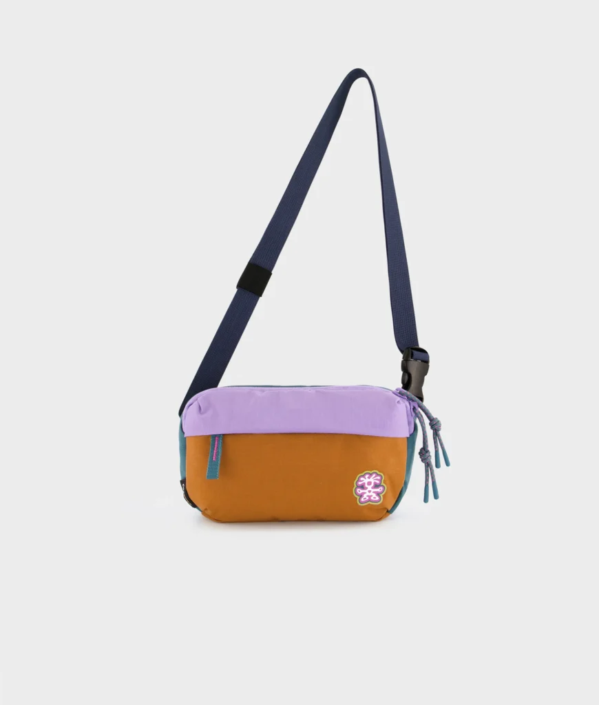 Wide Crumpler crossbody bag in camel and lavender tincture blocking displayed against a clean white background with a long adjustable shoulder strap