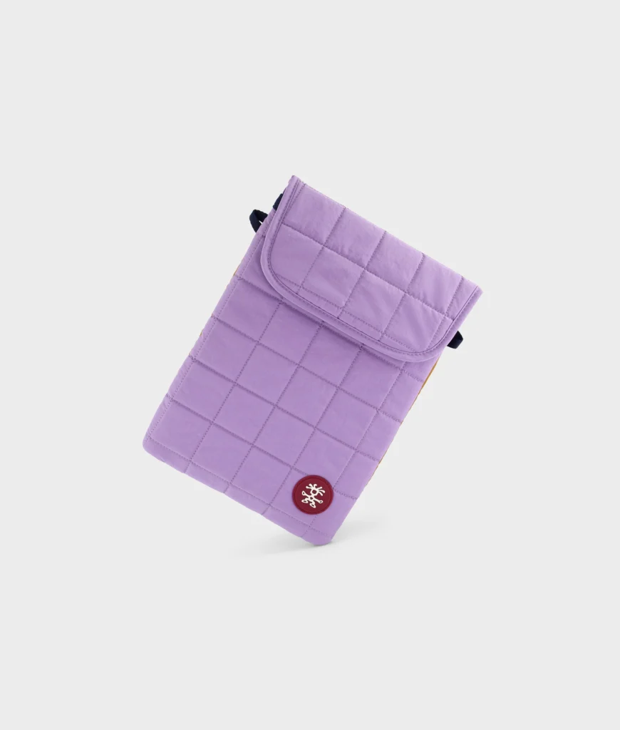 Lavender quilted Crumpler padded laptop sleeve displayed against a clean white background, featuring a flap closure, stitched grid pattern, and circular logo patch