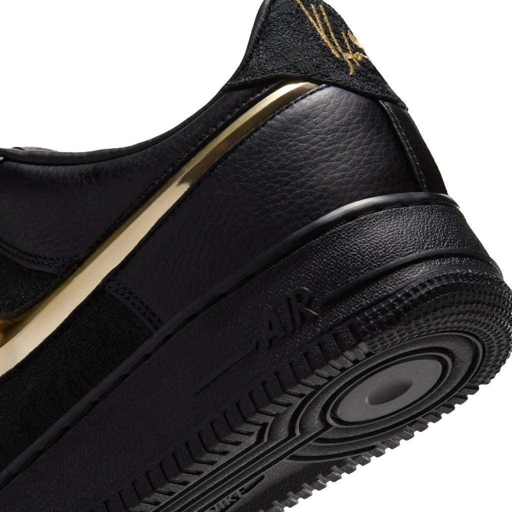 Detailed rear-quarter view of the Nike Air Force 1 highlighting the metallic gold Swoosh, premium black leather construction, embroidered Yoon heel brand, and black Air sole