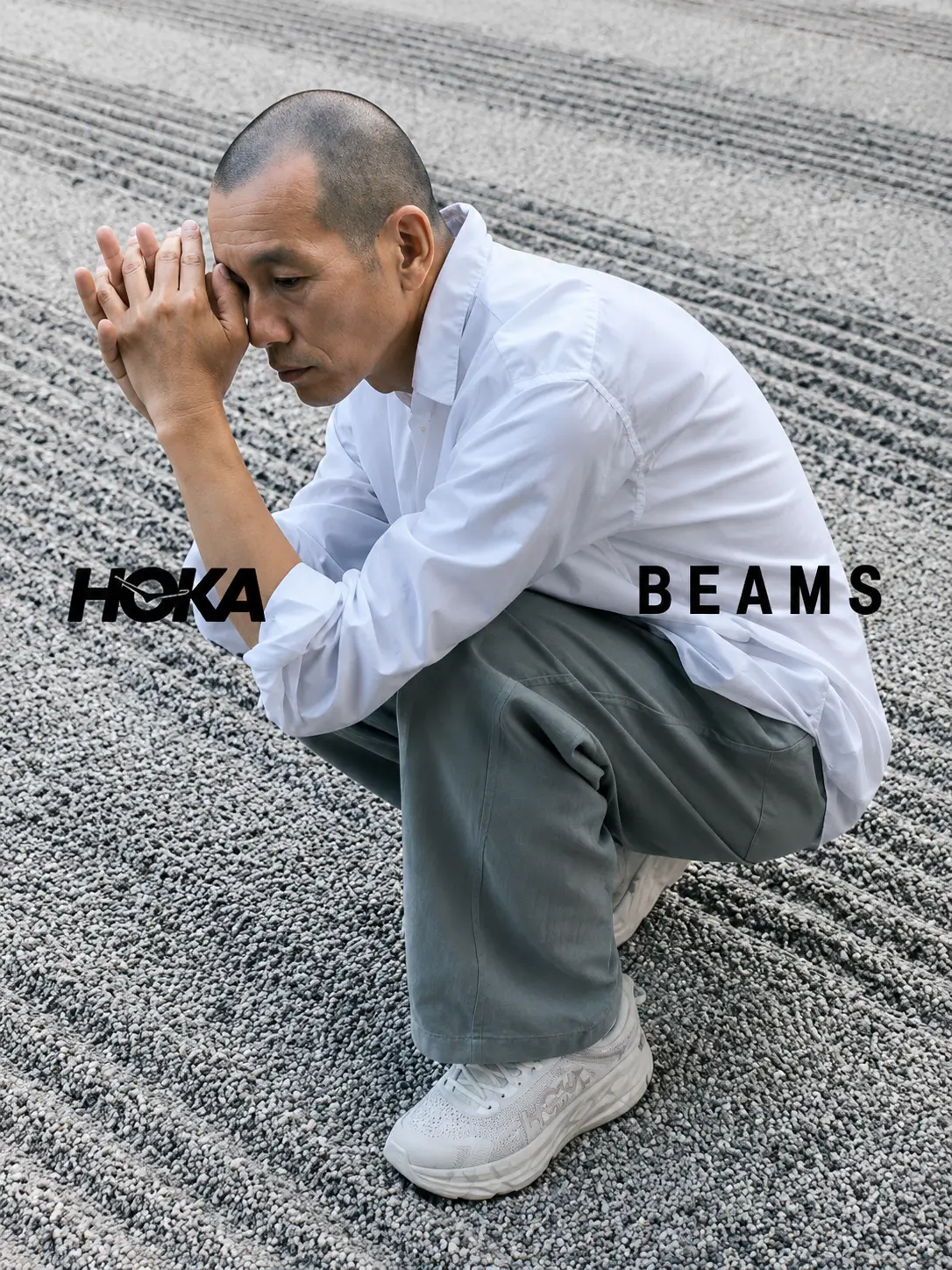 Campaign image of a crouching model in a white overshirt and loose gray trousers wearing off-white HOKA Project Transport shoes on raked gravel in a traditional Japanese Zen garden, with HOKA and BEAMS logos.