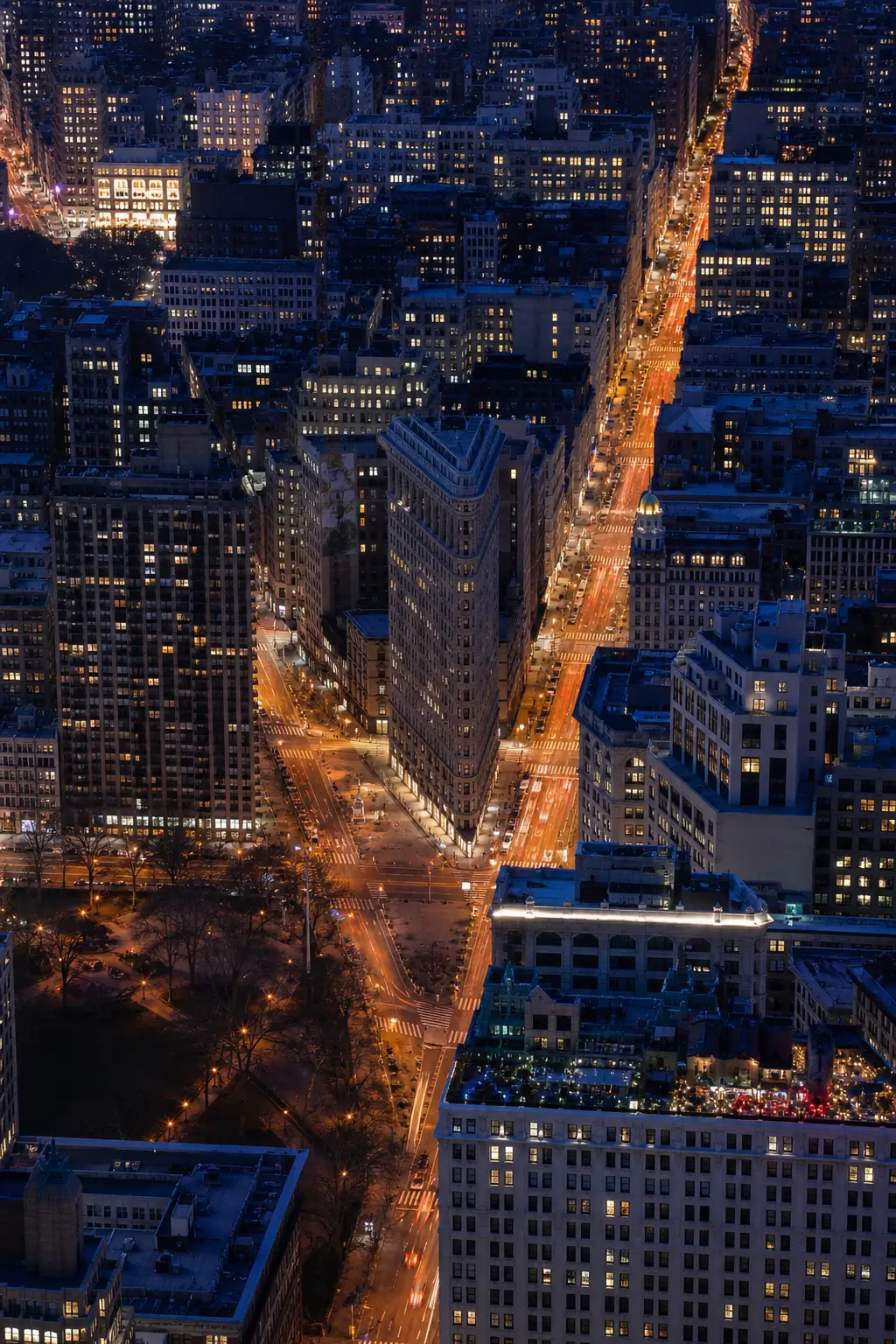 Aerial night view of Manhattan centered on the Flatiron Building, with glowing streets and illuminated skyscrapers.