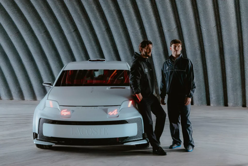 Pierre Niney and Pierre Gasly standing beside the Alpine A290 Rallye in a modern industrial space, wearing Alpine x Lacoste apparel with the rally-inspired concept car displayed front and center