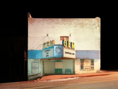 Historic Gem Theater illuminated at night along a quiet main street, featuring a glowing vintage marquee against a dark sky
