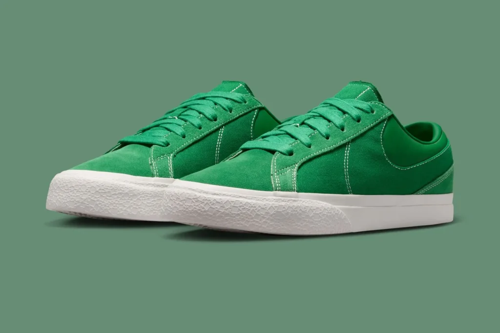 Angled view of the green Nike shoe highlighting the mixed suede and canvas upper, contrast stitching, textured rubber foxing, and clean white sole