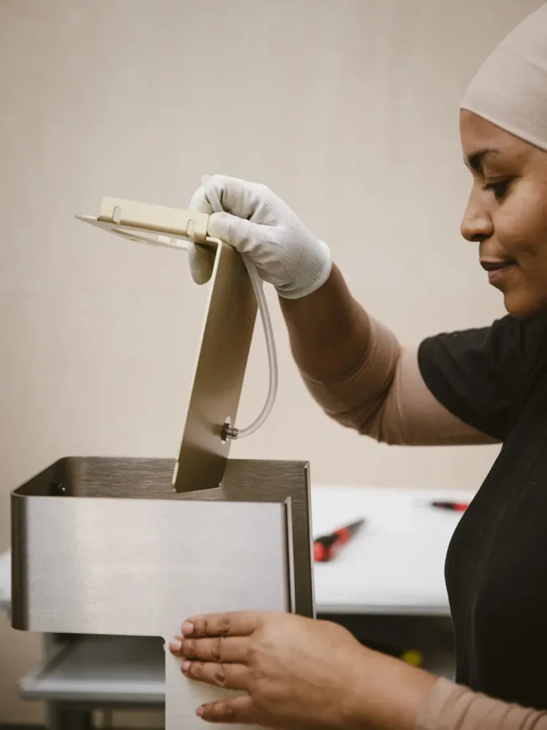 Factory worker carefully installing the top assembly of a brushed stainless steel espresso machine while wearing protective gloves during production
