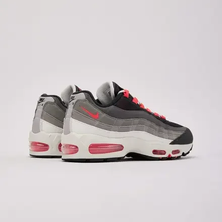 Pair of Nike Air Max 95 Big Bubble 'Solar Red' sneakers displayed from the rear three-quarter angle, featuring gradient grey suede overlays, black mesh uppers, Solar Red Swooshes, oversized visible Air units, and off-white midsoles.