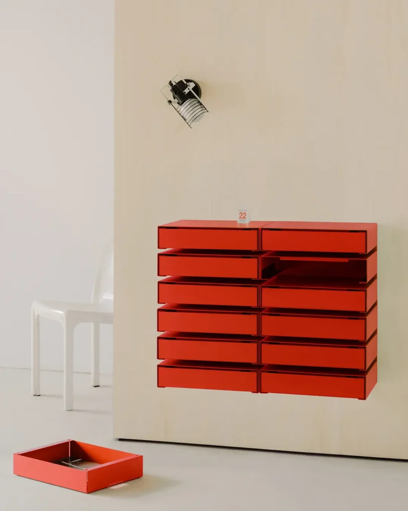 Wall-mounted modular red storage drawers displayed in a minimalist interior with a matching drawer removed and placed on the floor