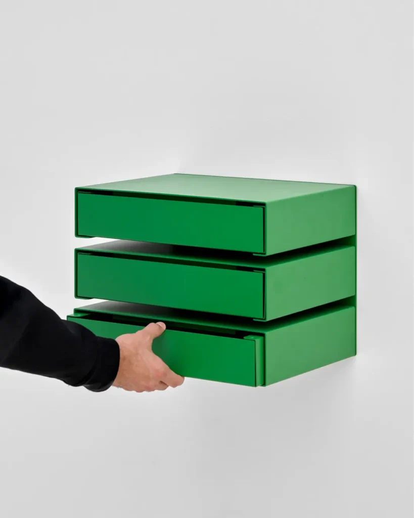 Green wall-mounted modular storage drawers with a hand opening the bottom drawer to demonstrate the pull-out design