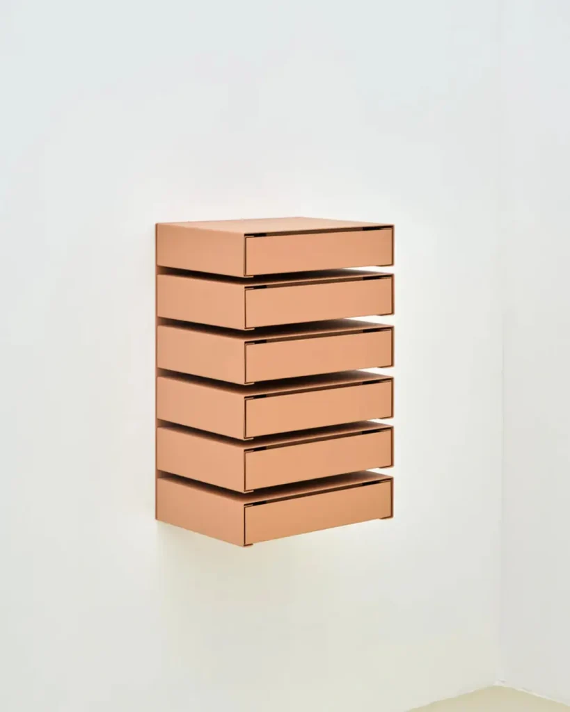 Peach-colored wall-mounted modular drawer unit shown against a clean white wall in a minimalist sett