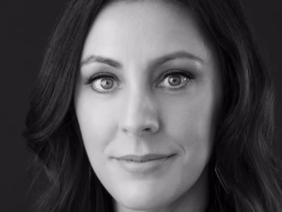 Black-and-white close-up headshot of Kathleen Van Nest Pierce with long dark hair, looking directly into the camera with a slight smile against a dark studio background