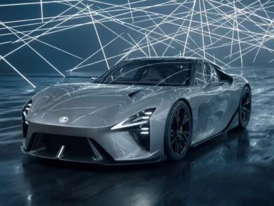 Front three-quarter studio view of the Lexus Electrified Sport concept beneath a ceiling of intersecting LED light bars, emphasizing its sculpted hood, aggressive front fascia, slim headlights, and sleek electric supercar silhouette reflected across the glossy floor