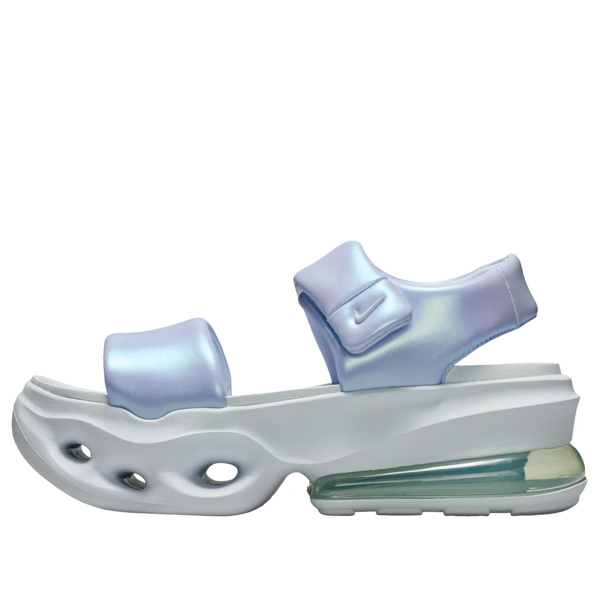 Side profile of the Nike Air Max Muse sandal in a shimmering iridescent light blue finish. The futuristic sandal features a molded white foam platform with sculpted ventilation cutouts at the forefoot, a visible Air Max unit in the heel with a translucent pale green tint, an open toe strap, and an adjustable ankle strap with a tonal mini Swoosh logo, shown against a clean white background.