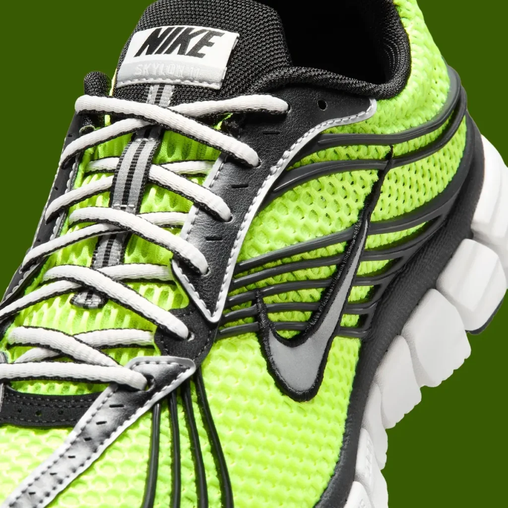 Close-up of the Nike Zoom Skylon 11 lateral side featuring metallic silver Swoosh branding, black molded overlay cage, volt honeycomb mesh upper, white laces, and Nike Skylon 11 tongue label